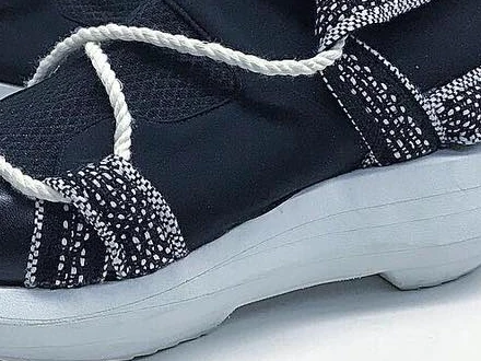 Close-up of black and white woven straps crossing a neoprene upper above a black leather toe